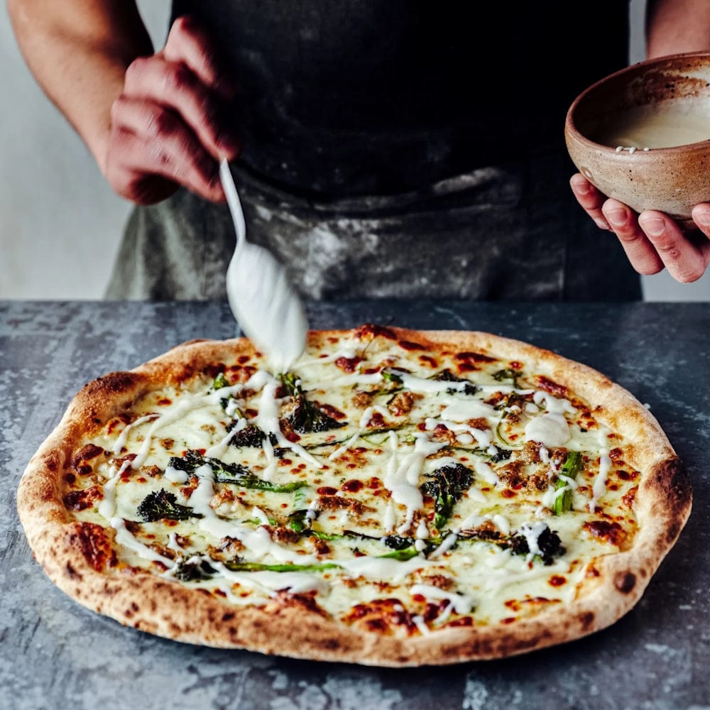 a person pouring sauce on pizza from Gozney Pizza Cookbook Volume 01