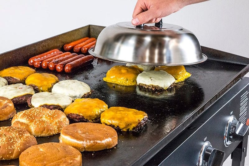 a Blackstone - 12" Basting Cover used to melt cheese over burger patties on a griddle
