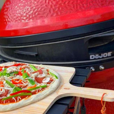 An uncooked pizza on a kamado joe pizza peel placed on top of a KJ grill shelf