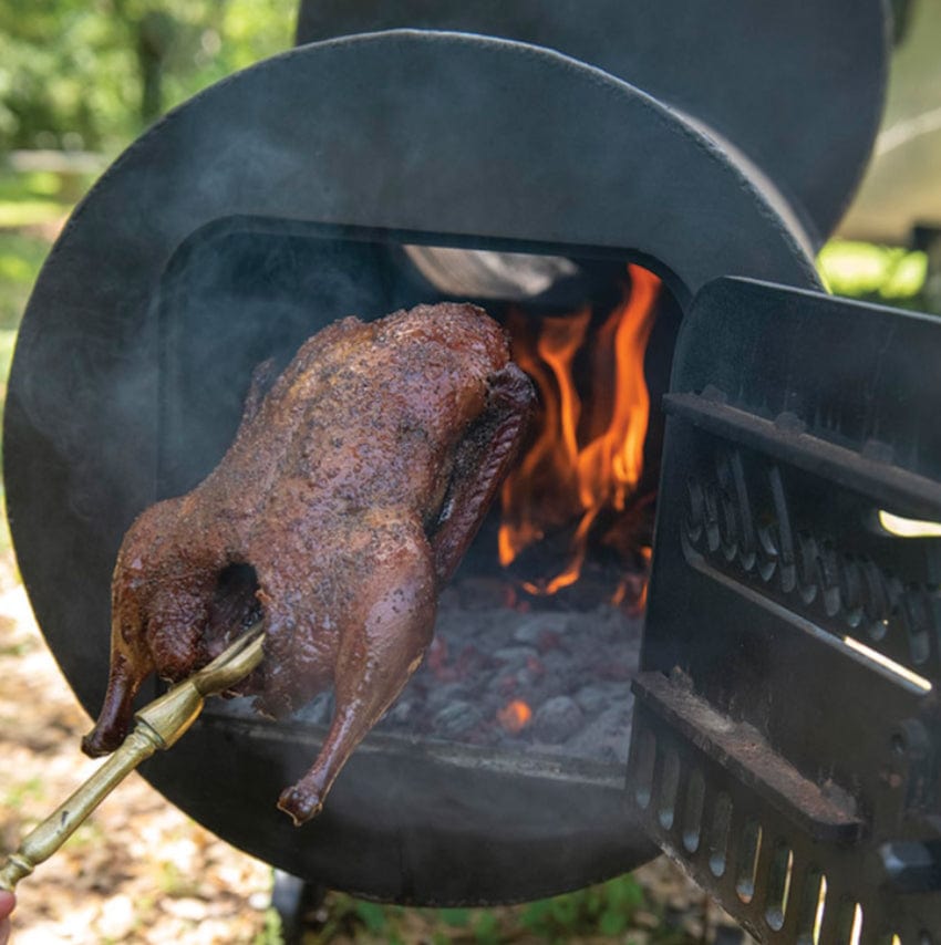 Getting out a skewered roast duck through the firebox's lid of a Franklin Pit